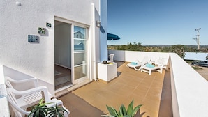 Un balcon avec des chaises blanches, une table et un parasol bleu.