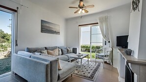 Un salon moderne avec un canapé gris, une table basse, un ventilateur de plafond, un téléviseur et une cheminée.