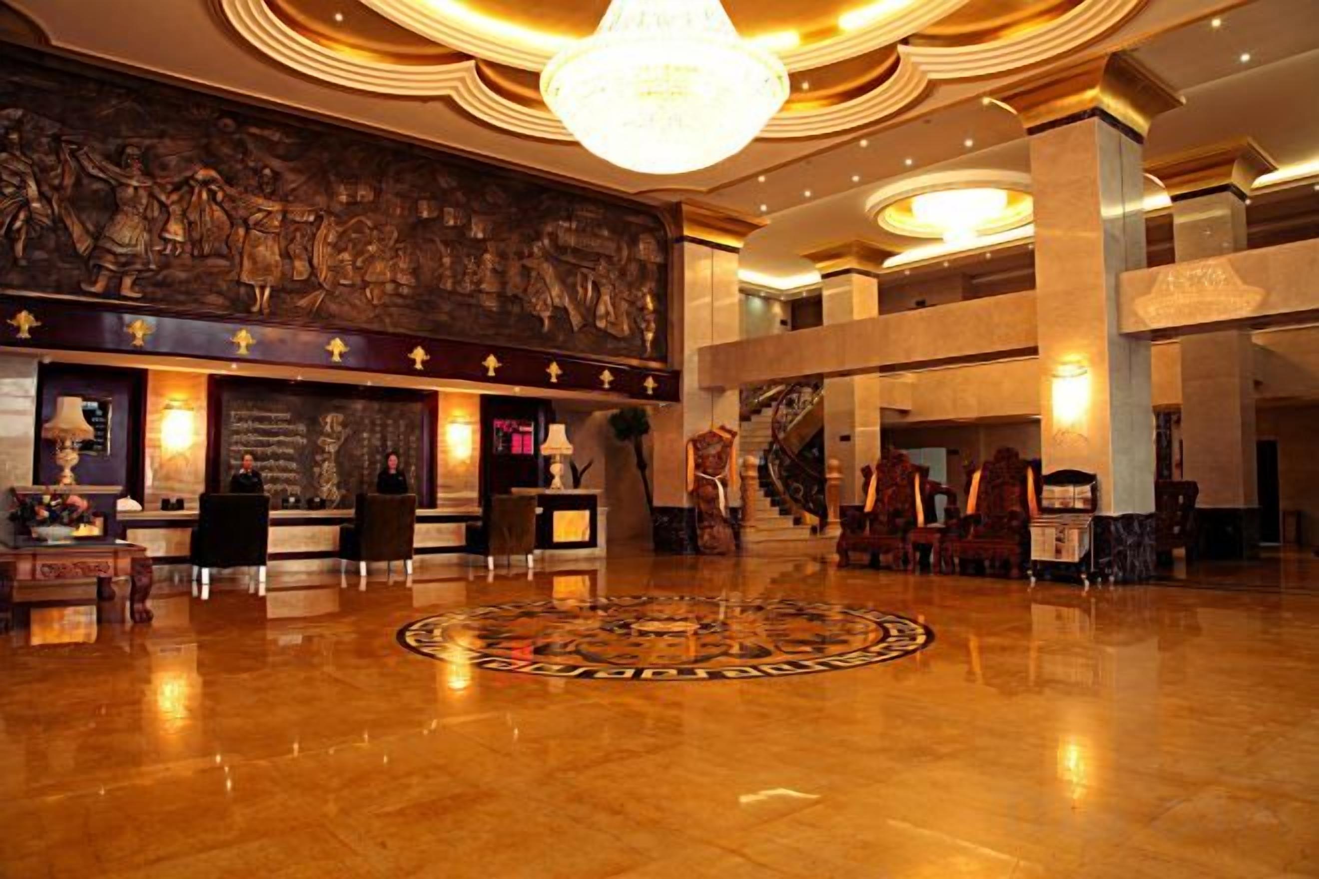 A spacious lobby with a grand chandelier, a reception desk, and a large mural on the wall.