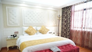 A bedroom with a large bed, a red bench, a nightstand, and a mirror. - Dele Grand Hotel (Xiangcheng)