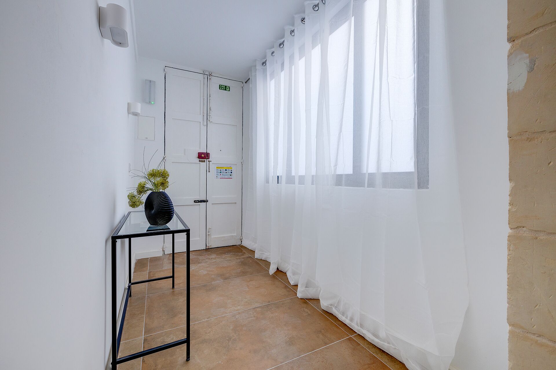 A hallway with a glass table, a white door, and a window with sheer curtains.