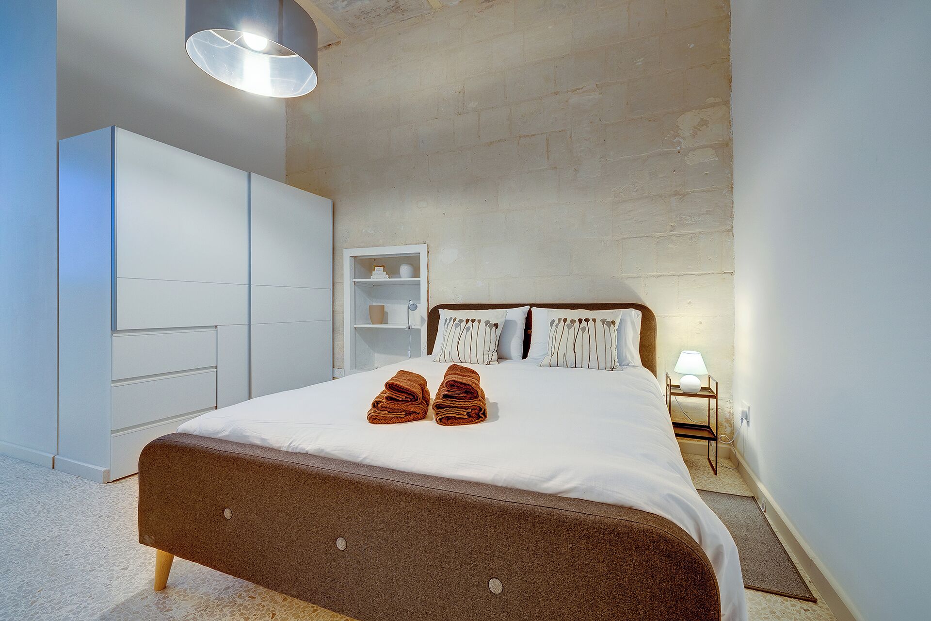 A bedroom with a bed, a wardrobe, a bedside table, and a lamp.