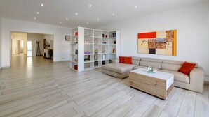 Una sala de estar moderna con suelo de madera, un sofá color beige, un estante blanco y una mesa de centro de madera.