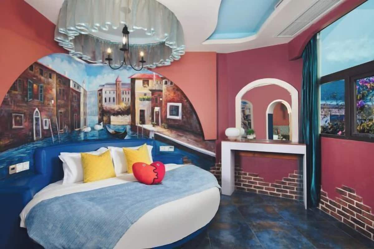 A room with a bed, a desk, a mural, and a view through a window.