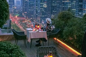 An outdoor dining area with a table set for two, surrounded by greenery and overlooking a cityscape. - Style Fashion Hotel (Linshui Hongfan Square County Government Branch) (Linshui)