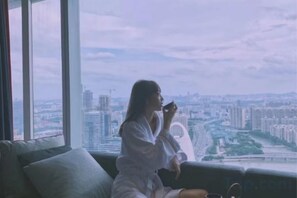 A person sitting on a couch by a large window overlooking a cityscape. - Style Fashion Hotel (Linshui Hongfan Square County Government Branch) (Linshui)