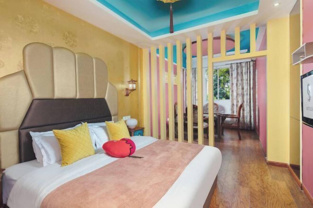A hotel room with a bed, a nightstand, a TV, and a view of the outdoors.