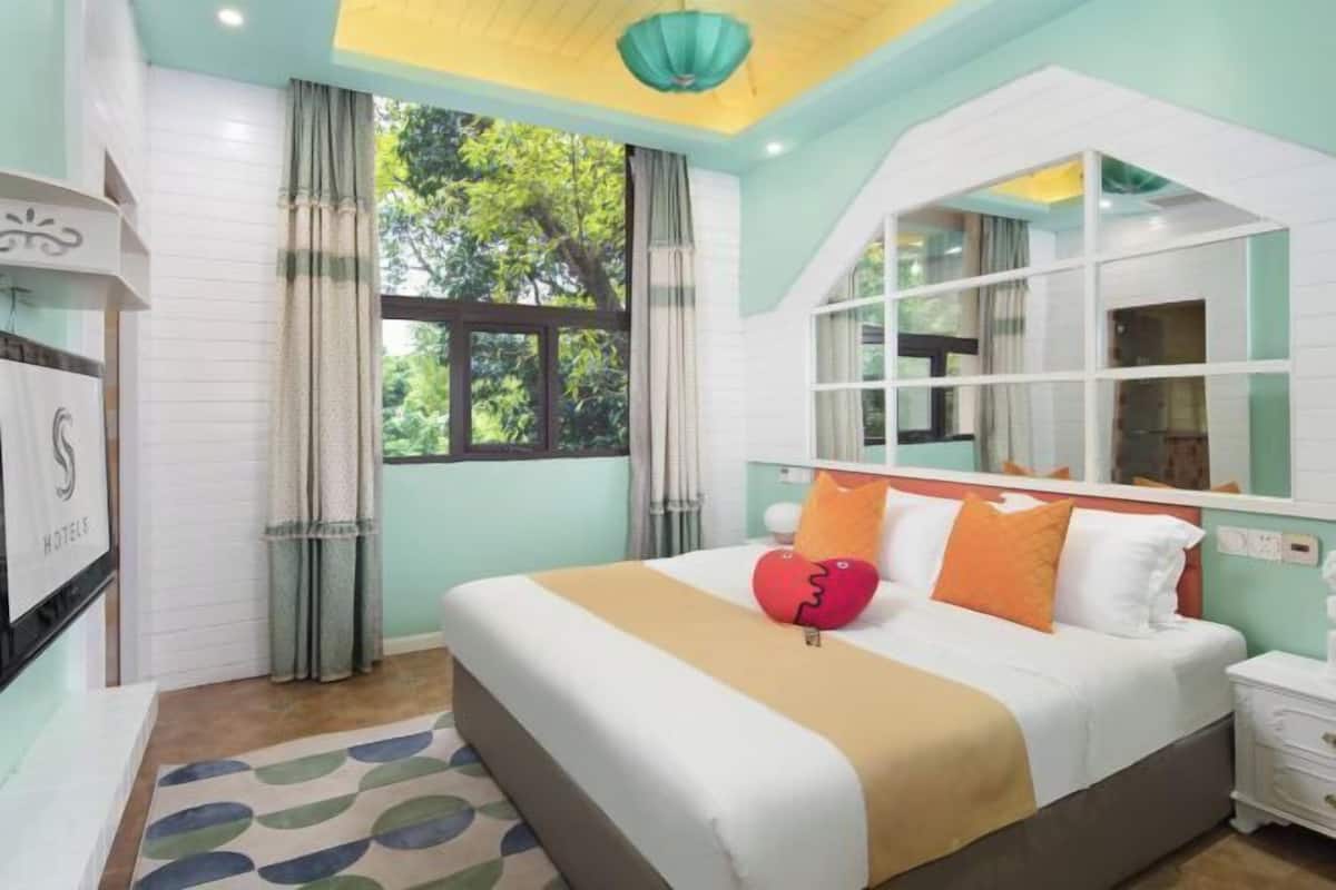 A bedroom with a bed, a nightstand, a mirror, and a window with curtains.
