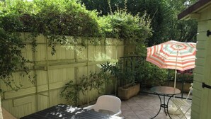 Un patio con una mesa y sillas, un paraguas a rayas y una cerca verde.