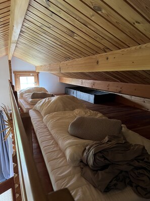 Una habitación tipo dormitorio con literas, vigas de madera en el techo y una ventana con vistas.