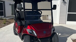 Une voiturette de golf rouge est garée devant une maison avec un garage.