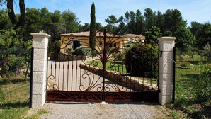 Una reja de hierro forjado con diseños intrincados, que da acceso a un edificio con tejado de baldosas y pilares de piedra.
