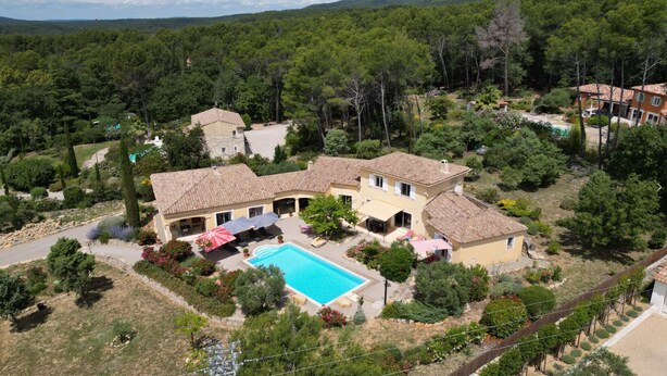 Una amplia villa con piscina, rodeada de exuberante vegetación y varias construcciones.