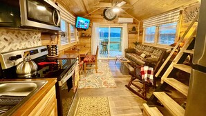 A compact kitchen with a stove, microwave, and a TV mounted on the wall.