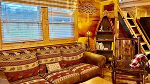 A cozy cabin interior with a wooden sofa, a bench, a bookshelf, and a ladder leading to a loft.
