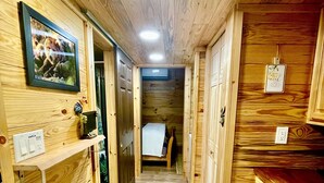 A narrow hallway with wooden walls and a tiled floor, leading to a bed with a white sheet.