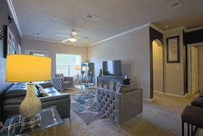 A living room with a sofa, armchair, and ottoman, a television, and a ceiling fan.
