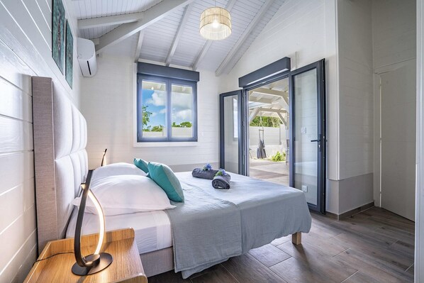 Une chambre à coucher comprenant un lit, une table de chevet avec une lampe, une fenêtre donnant sur un paysage agréable et une porte-fenêtre coulissante qui mène à un espace extérieur.