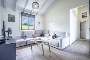 Un salon moderne avec un canapé gris, une table basse en verre et une grande fenêtre.