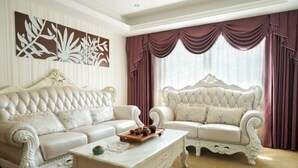 A room with two ornate white sofas, a white coffee table, and a large window with purple curtains.