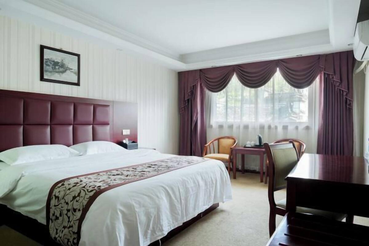 A hotel room with a large bed, a wooden headboard, a small table, and a chair.