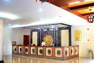 Un área de recepción con una pared de mármol, un espejo decorativo grande y un mostrador de recepción con paneles estampados.