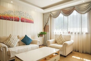 A well-lit living room with a beige sofa, a white coffee table, and a painting on the wall. - Yaoli Holiday Hotel (Fuliang)