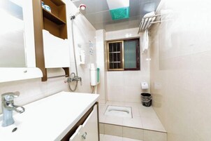 Casa de banho com uma pia branca, espelho, chuveiro e sanita.
