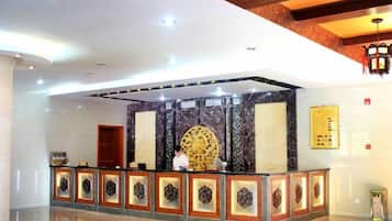 A reception area with a marble wall, a large circular decorative piece, and a reception desk with patterned borders.