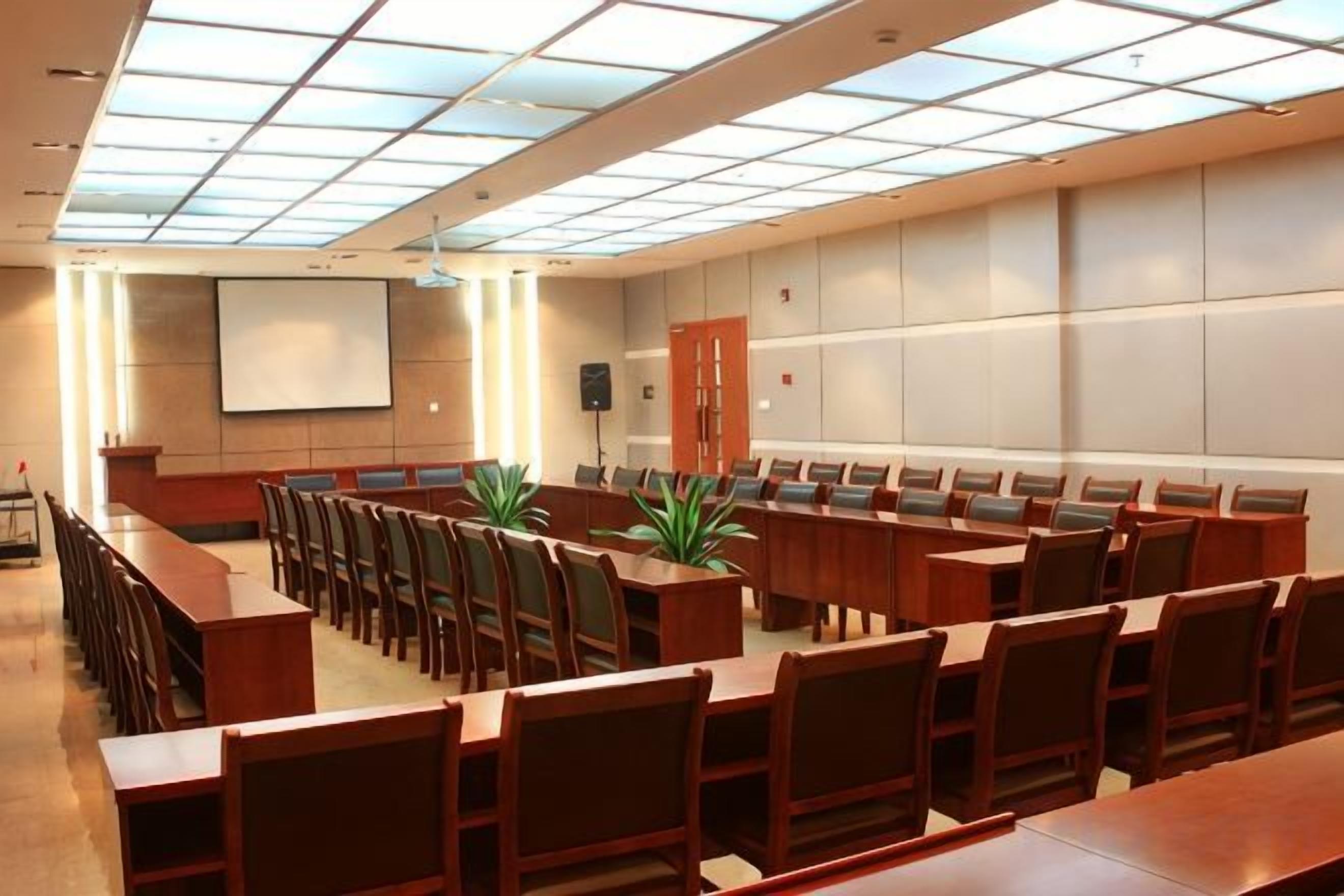 Un salón de conferencias con una larga mesa y sillas, una pantalla de proyector y un amplio ventanal con diseño de cuadrícula.