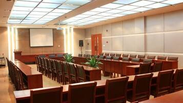 Un salón de conferencias con una larga mesa y sillas, una pantalla de proyector y un amplio ventanal con diseño de cuadrícula.