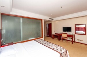 Quarto de hotel com uma cama grande, uma escrivaninha com cadeira, televisão e um espelho na parede.
