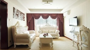 A living room with a white sofa, a white armchair, a white coffee table, and a television on the wall.