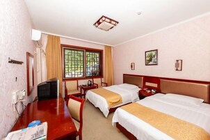 Quarto de hotel com duas camas, uma mesa, uma cadeira, televisão e janela com cortinas.