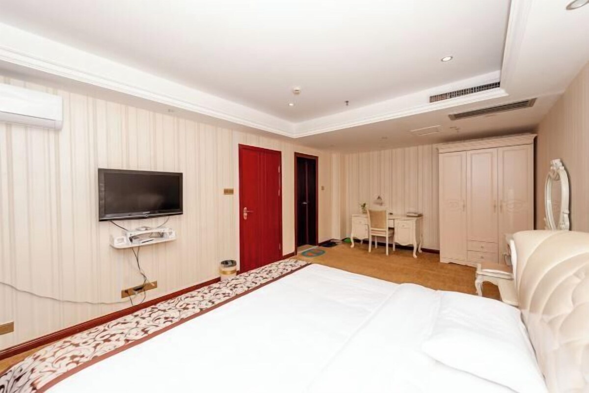 A hotel room with a bed, a television mounted on the wall, a desk, and a wardrobe.