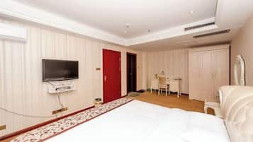 A hotel room with a bed, a television mounted on the wall, a desk, and a wardrobe.