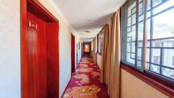 A hotel corridor with red doors, a floral carpet, and large windows.