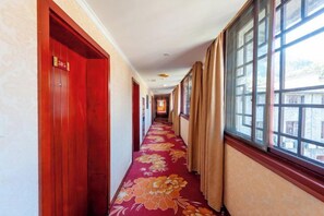 Een hotelgang met rode deuren, een bloemenprint tapijt en grote ramen.