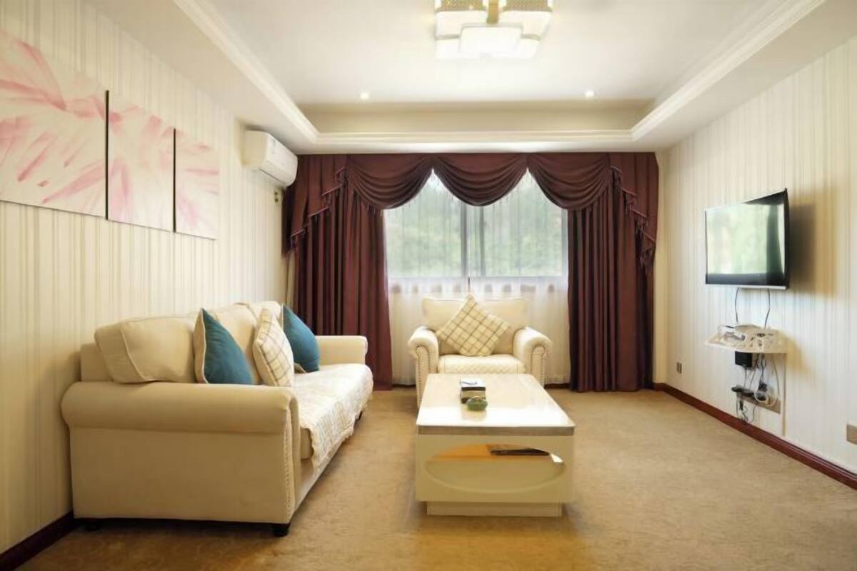 A living room with a sofa, armchair, coffee table, TV, and curtains.