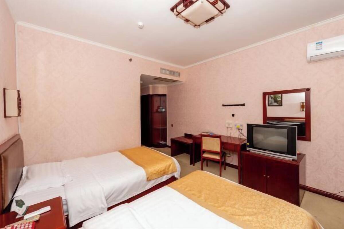 A hotel room with two beds, a desk, a television, and a mirror.