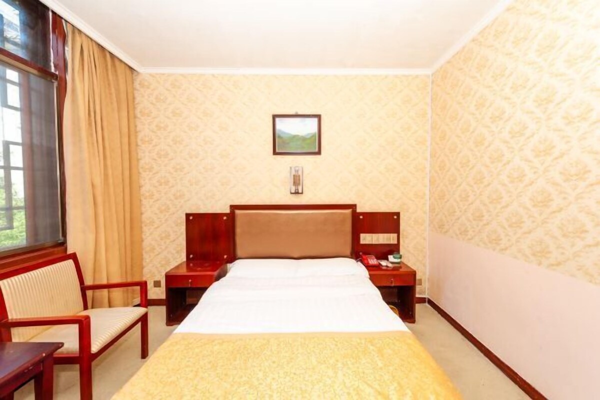 A hotel room with a bed, a chair, a nightstand, and a window with curtains.