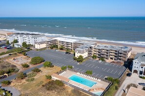 An aerial view of a coastal hotel with multiple buildings, a parking lot, and a swimming pool.