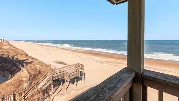 A beach view from a wooden balcony with a wooden staircase leading down to the beach. - Golden Strand Unit C3: Oceanfront | Shared Pool (Kill Devil Hills)