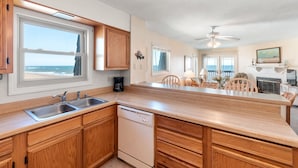 A kitchen with wooden cabinets, a dishwasher, and a large window overlooking the ocean. - Golden Strand Unit C3: Oceanfront | Shared Pool (Kill Devil Hills)