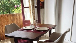A dining area with a table set for two, two chairs, and a view of greenery outside.
