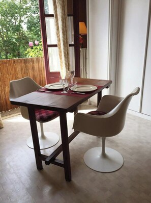 Un coin repas avec une table dressée pour deux personnes, deux chaises et une vue sur la verdure environnante.