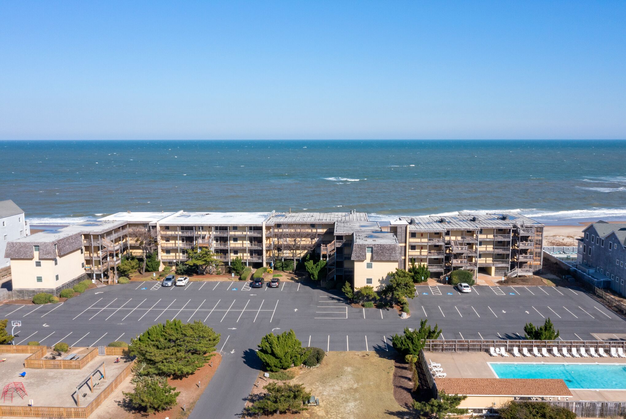 Hotel a la platja amb múltiples balcons, un aparcament i una piscina.