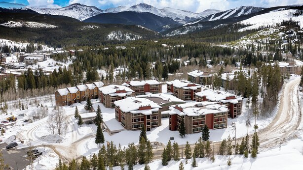 A snow-covered resort with multiple buildings, a ski trail, and mountains in the background. - Silverado II Unit 334 Great views clubhouse amenities bedding for 2 couples (Winter Park)