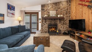 A cozy living room with a stone fireplace, a television, and a blue sofa. - Silverado II Unit 334 Great views clubhouse amenities bedding for 2 couples (Winter Park)