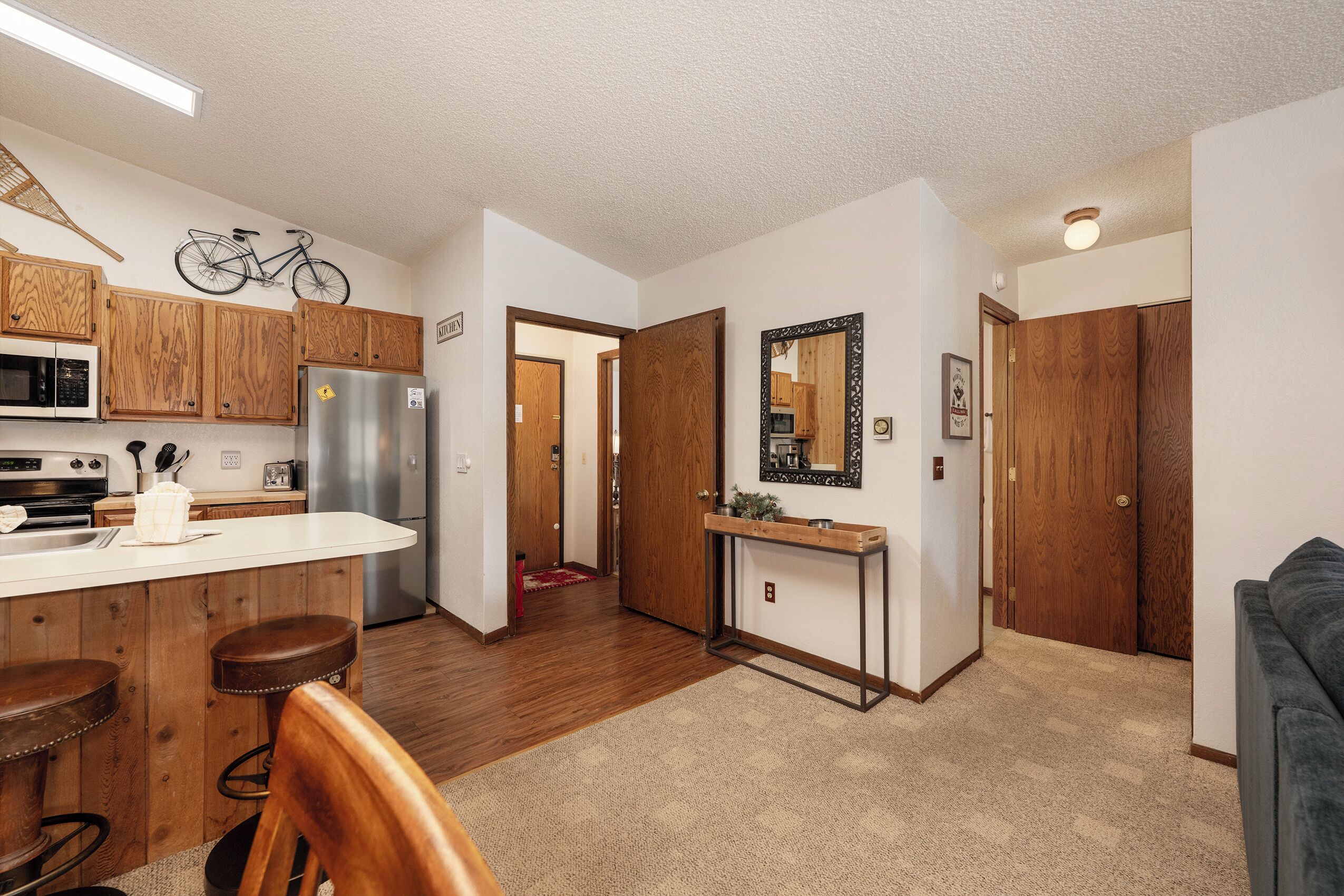 A modern kitchen with wooden cabinets, a stainless steel refrigerator, and a bar area with stools.